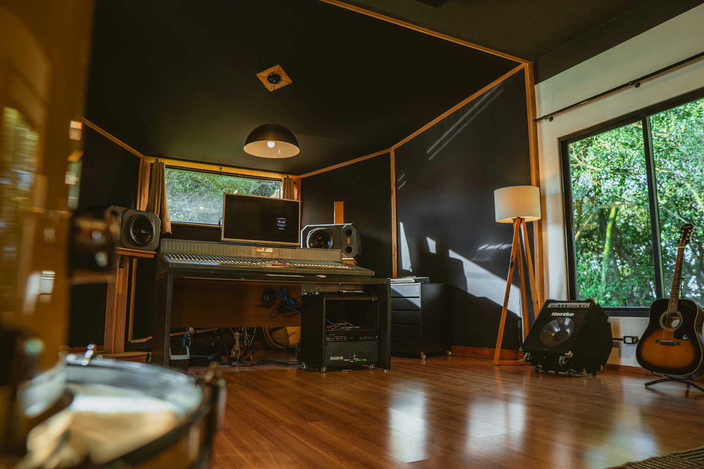 Musikstudio mixerbord med gitarr och förstärkare vid fönstret.